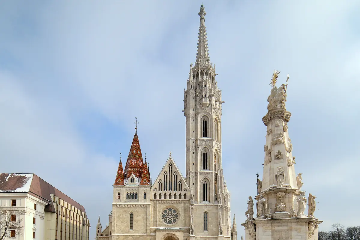 Kostel svatého Matěje na zasněženém náměstí s vysokou věží, taškovými štíty a bílým sloupem Nejsvětější Trojice vpravo